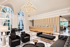 A modern lobby with a reception desk, seating area, and a large chandelier.