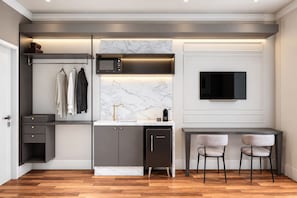 Una cocina moderna con microondas integrado, un lavamanos con grifo dorado, un refrigerador negro y un comedor con dos sillas.