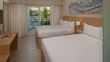 Habitación de hotel con dos camas, un escritorio, televisión y balcón con vista a palmeras.