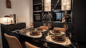Una cocina moderna con encimera de mármol, horno empotrado y zona de comedor preparada con platos y vasos.