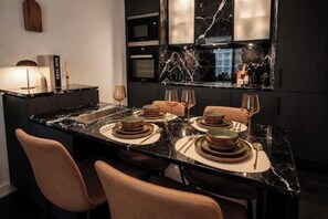 A modern kitchen with a marble countertop, built-in oven, and a dining area set with plates and glasses. - Luxury Yorkville Condo Sleeps 3 (Toronto)