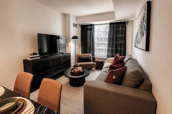 A modern living room with a sofa, a coffee table, a TV, and a dining area with chairs and a table. - Luxury Yorkville Condo Sleeps 3 (Toronto)