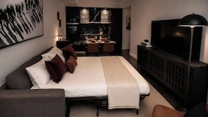 Un dormitorio moderno con una cama grande, un televisor y una zona de comedor al fondo.