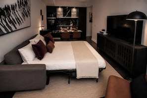 A modern bedroom with a large bed, a TV, and a dining area in the background. - Luxury Yorkville Condo Sleeps 3 (Toronto)