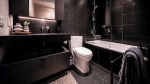 Un baño moderno con pared de azulejos blancos y negros, un inodoro blanco, un tocador negro y un área de ducha con cerramiento de vidrio.