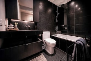 A modern bathroom with a black and white tiled wall, a white toilet, a black vanity, and a glass-enclosed shower area. - Luxury Yorkville Condo Sleeps 3 (Toronto)