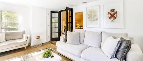 Una sala de estar moderna con un sofá blanco, una mesa de centro de vidrio y una puerta que da a otra habitación.