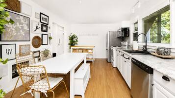 A modern kitchen with white cabinetry, stainless steel appliances, and a wooden dining table with wicker chairs.