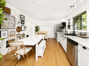 Una cocina moderna con armarios blancos, electrodomésticos de acero inoxidable y una mesa de comedor de madera con sillas de mimbre.