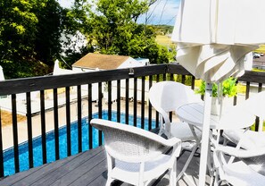 Une terrasse avec une piscine, des chaises en osier blanches et une table.