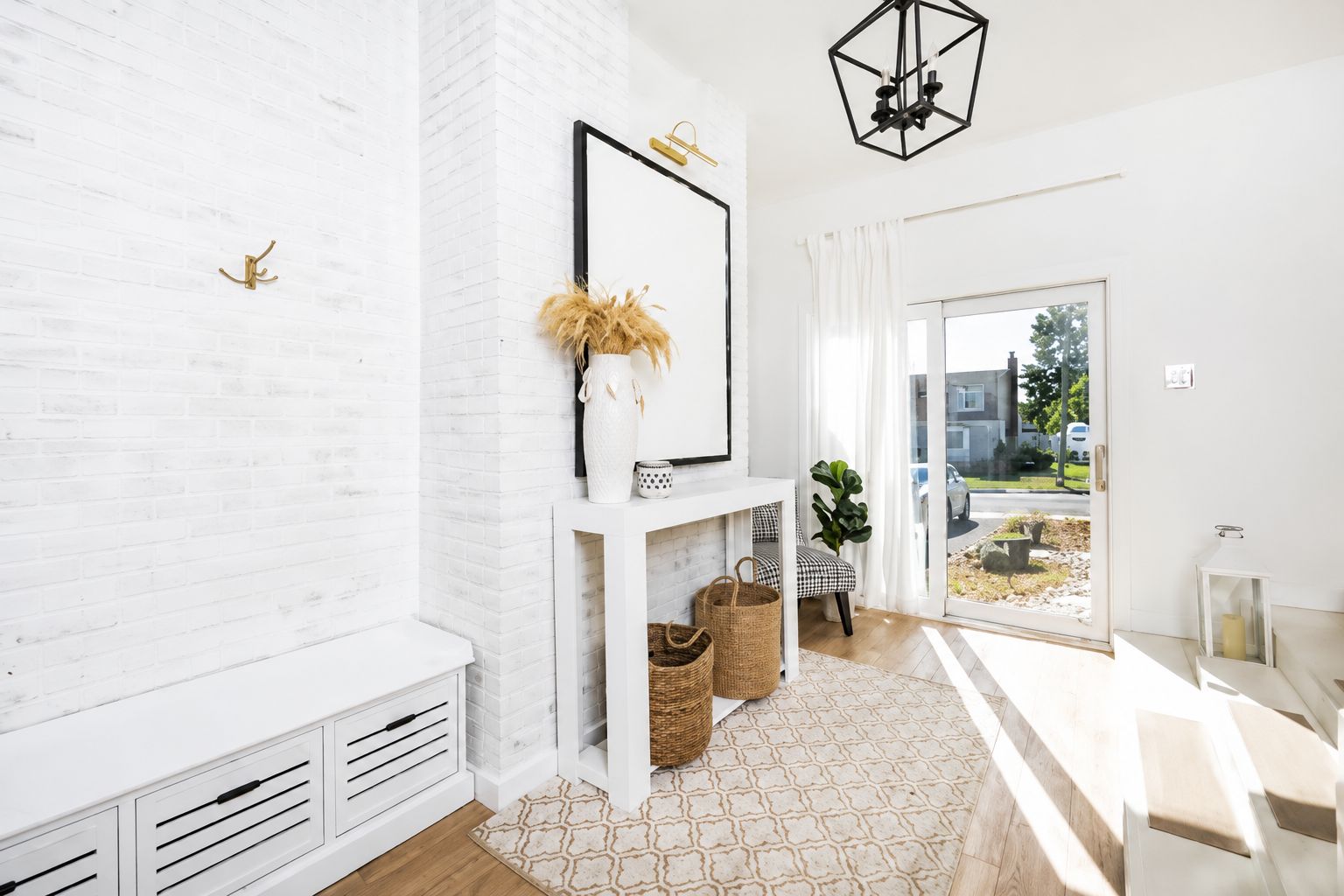 Ein modernes Interieur mit einer weißen Ziegelwand, einem weißen Konsolentisch mit Vase und Korb, einer Bank und Blick durch eine Glastür.