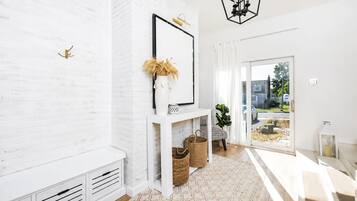 Ein modernes Interieur mit einer weißen Ziegelwand, einem weißen Konsolentisch mit Vase und Korb, einer Bank und Blick durch eine Glastür.