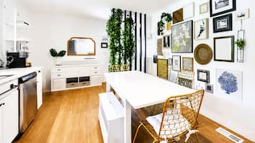Una cocina moderna con armarios blancos, lavavajillas integrado y un comedor con mesa blanca y una silla de mimbre.
