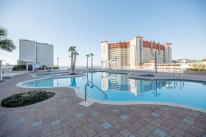A swimming pool with a tiled deck, surrounded by palm trees and a hotel building in the background. - Blue View Retreat at Laketown Wharf 720 - Ocean View, 3BR, Gym, Pools, Parking (Panama City Beach)