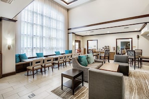 A hotel lobby with seating areas, a coffee station, and a dining area.
