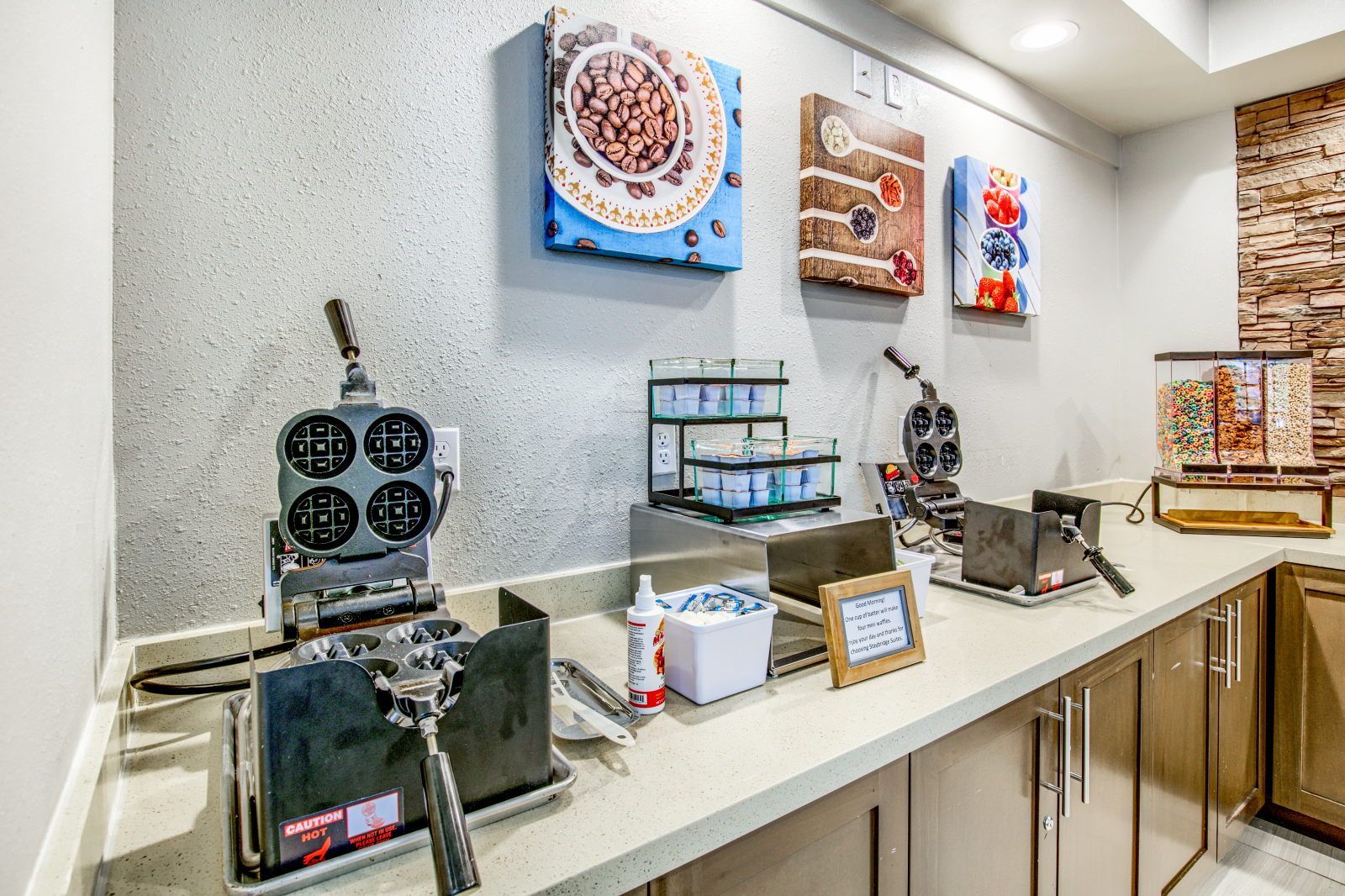 A breakfast bar with waffle makers, a coffee machine, and a variety of food containers.