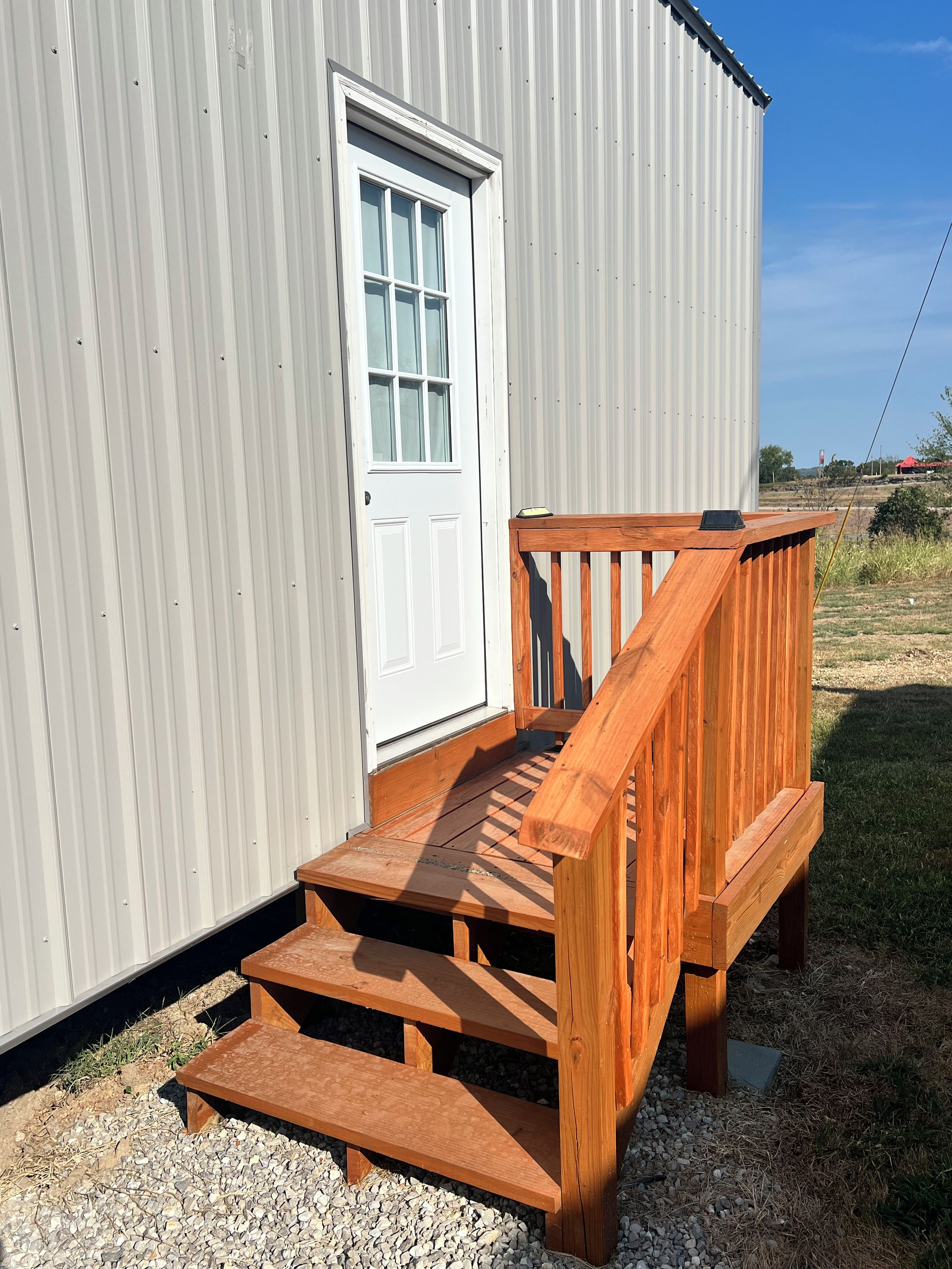 A wooden deck leading to a white door of a building with corrugated metal siding.