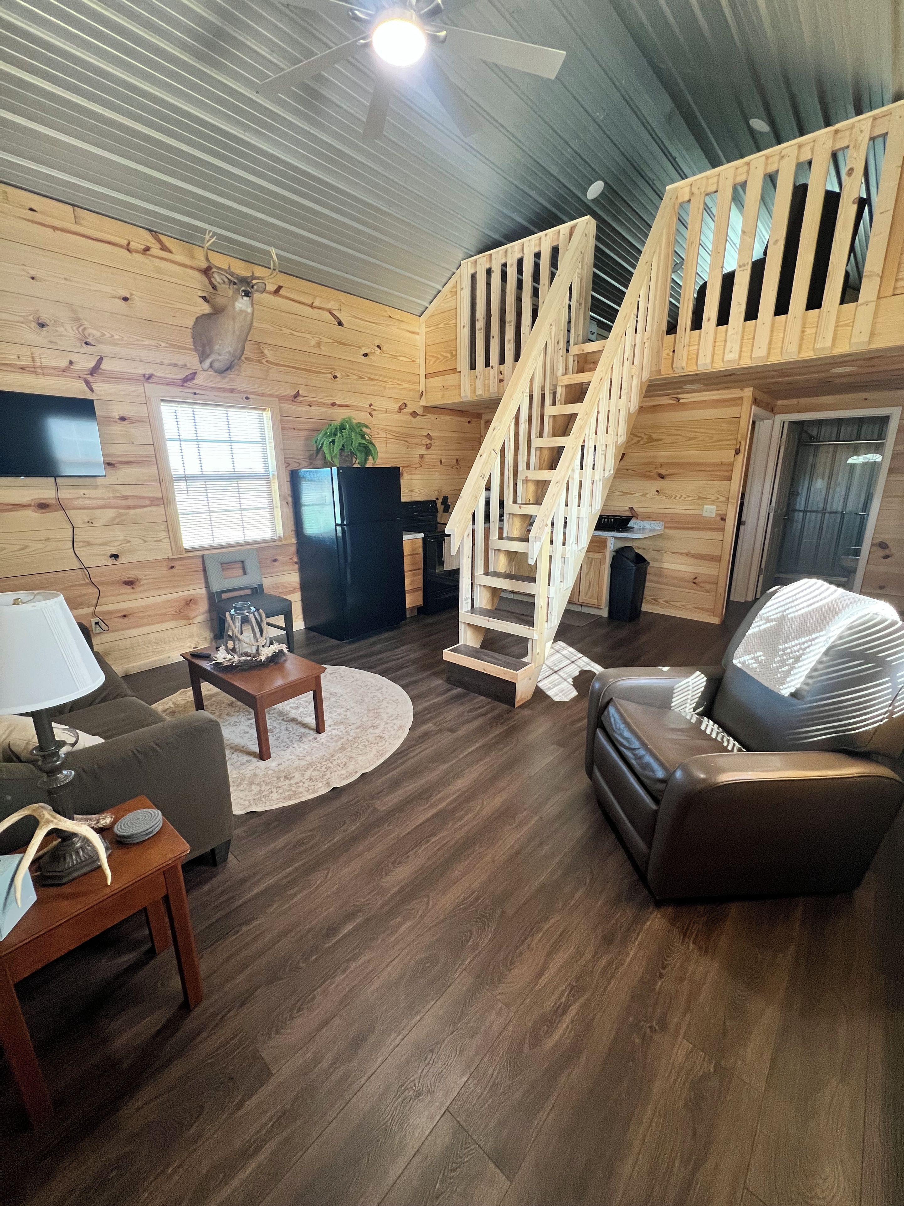 Ein gemütliches Blockhaushaus-Interieur mit einer Holztreppe, einem Flachbildfernseher, einem Kamin und einem Ledersofa.