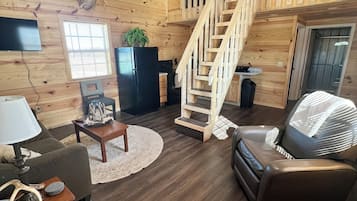 Ein gemütliches Blockhaushaus-Interieur mit einer Holztreppe, einem Flachbildfernseher, einem Kamin und einem Ledersofa.