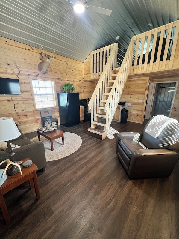 A cozy cabin interior with a wooden staircase, a flat-screen TV, a fireplace, and a leather sofa.