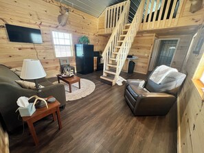 A cozy cabin interior with a wooden interior, a fireplace, a dining area, and a staircase.