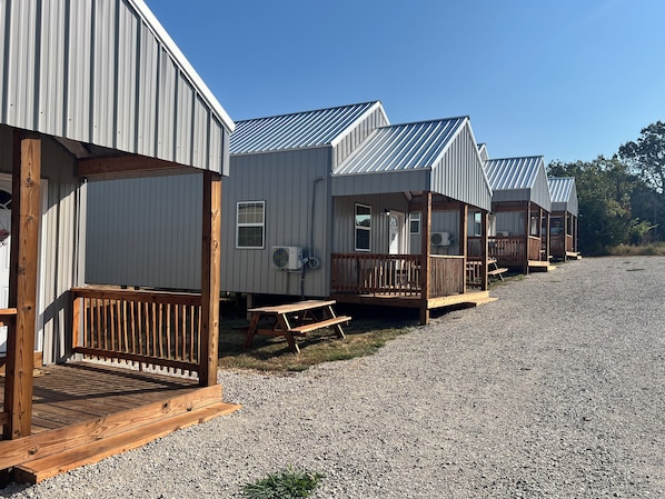 A row of small, single-story cabins with wooden decks and railings, each with a window and an air conditioning unit.