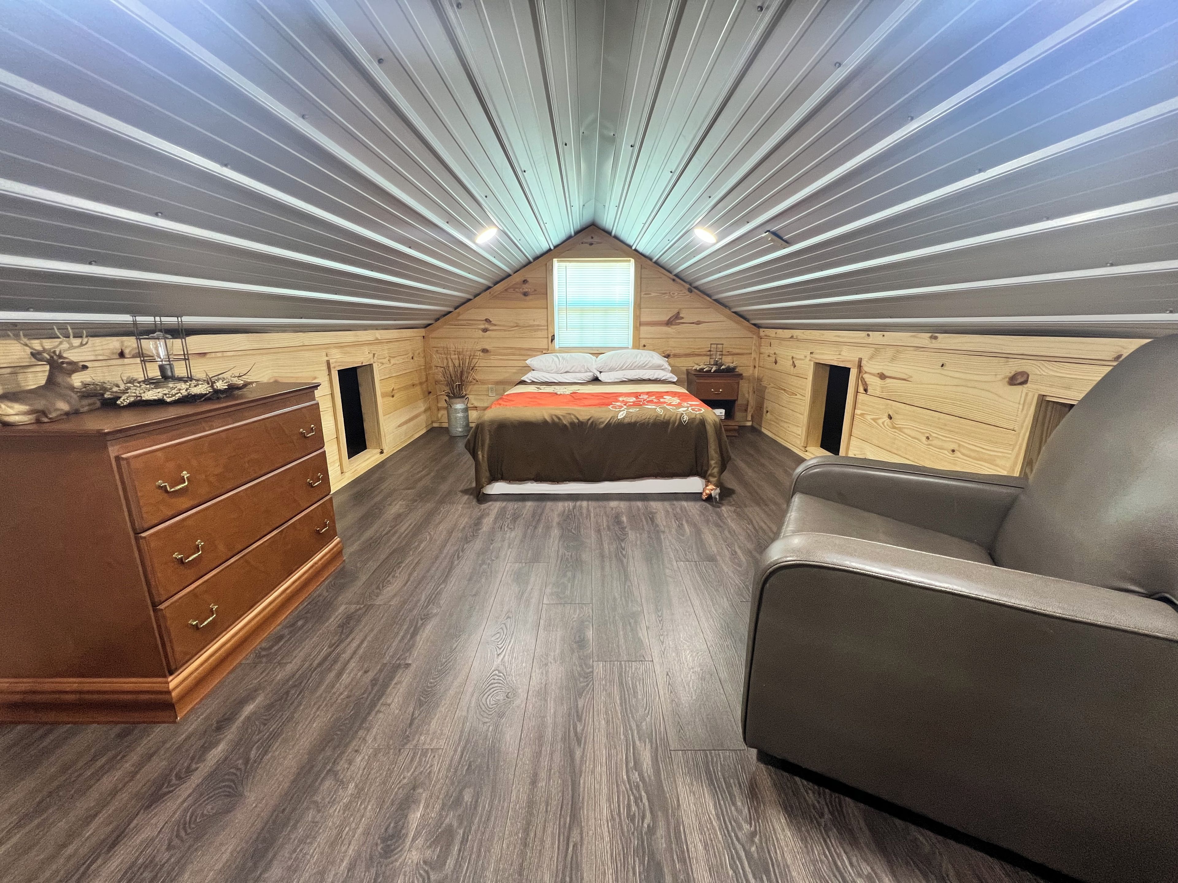 A bedroom with a sloped ceiling, a bed, a dresser, and a chair.