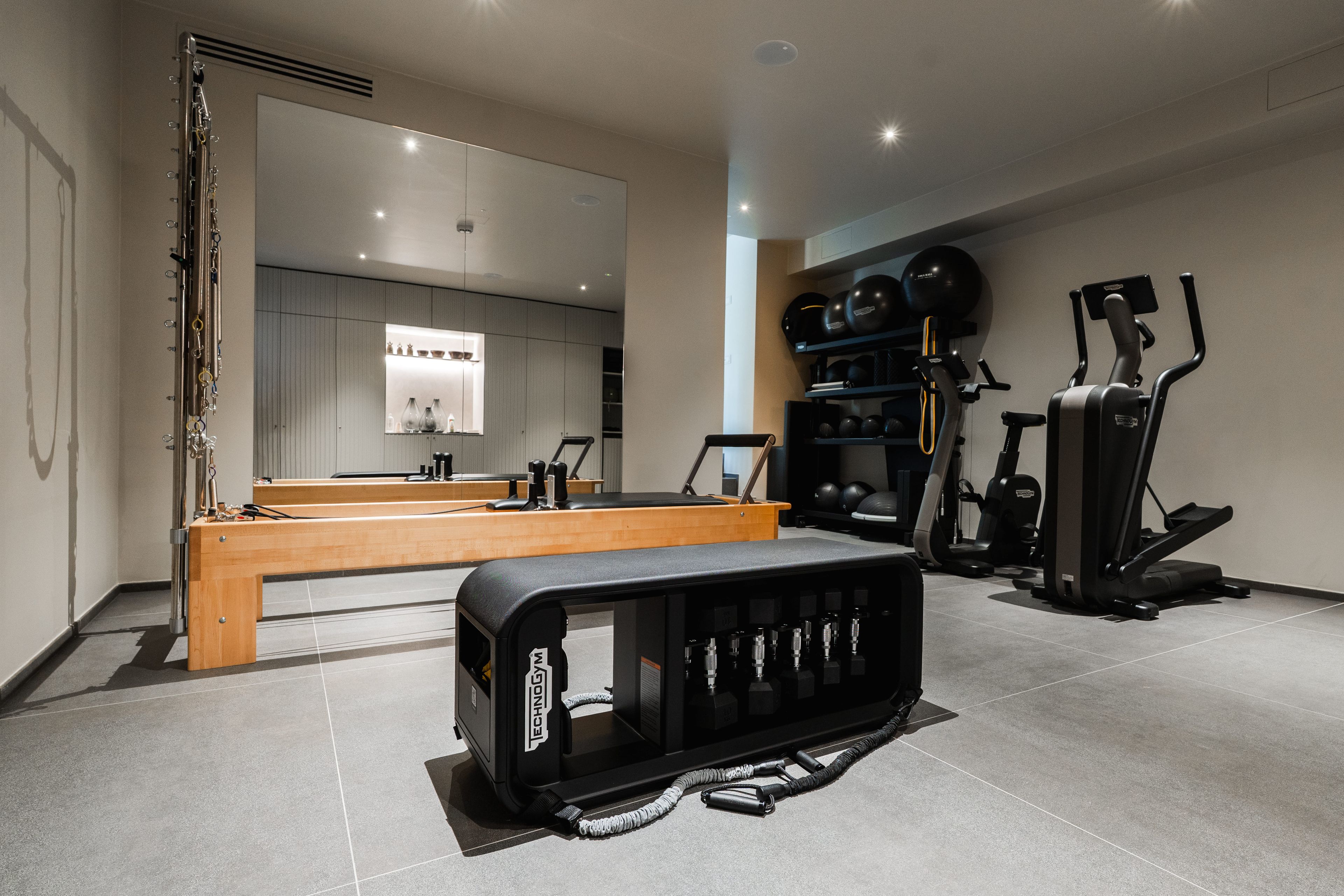 A modern gym with exercise equipment, a wooden bench, and a large mirror.
