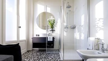 A modern bathroom with a glass shower enclosure, a round mirror, and a black and white patterned floor.