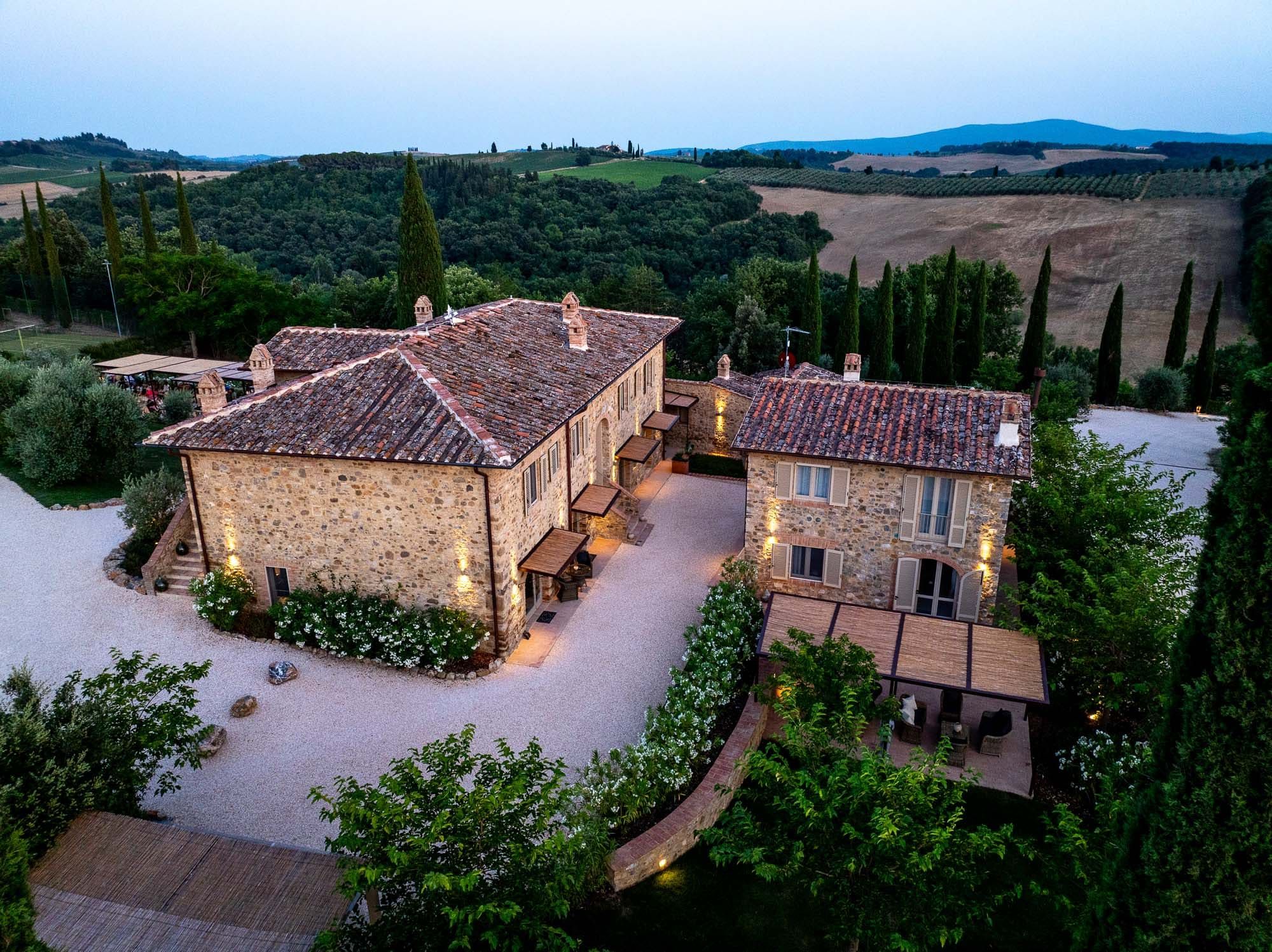 A stone villa with a courtyard, surrounded by trees and hills.