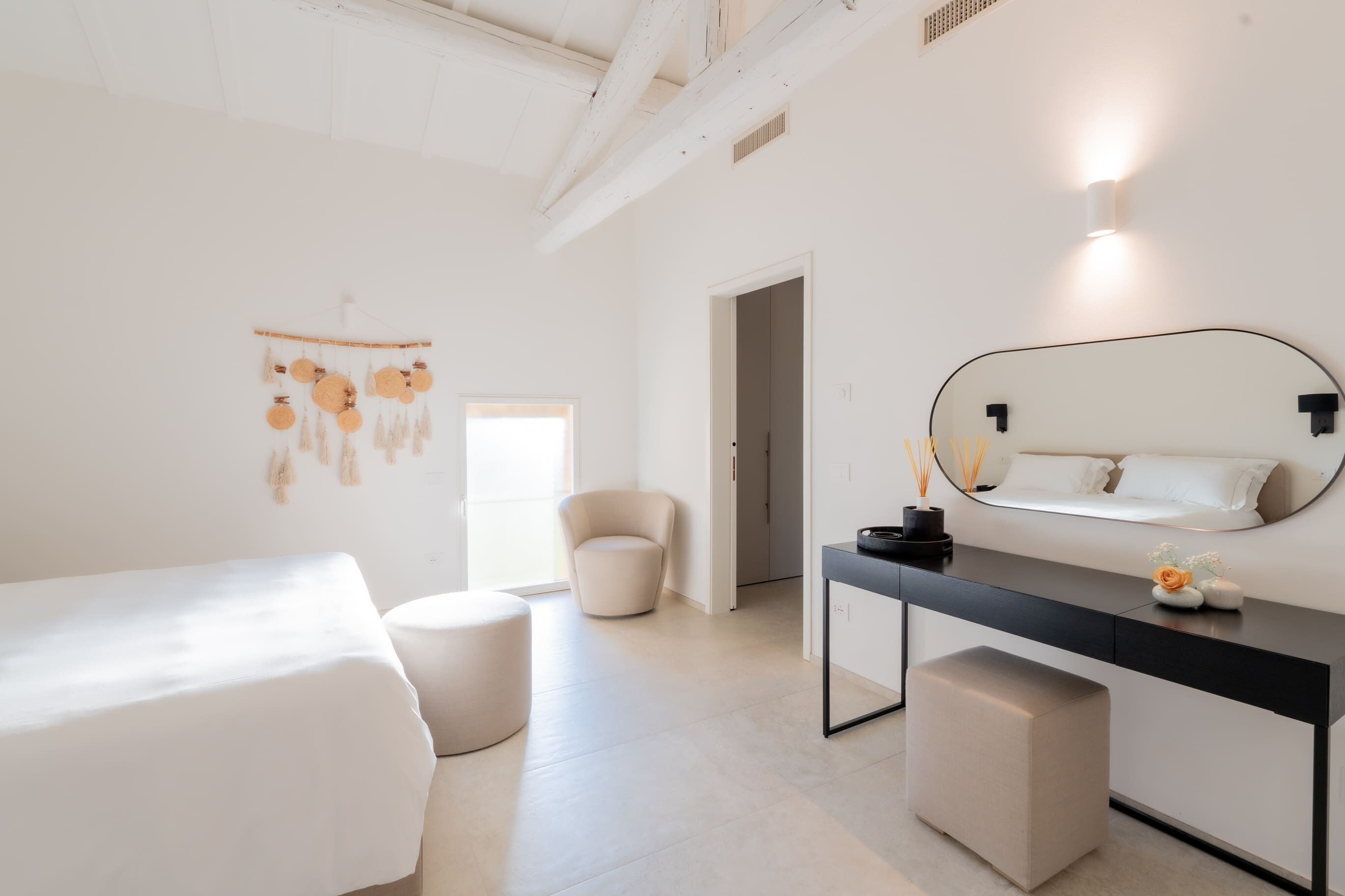 A minimalist bedroom with a bed, a chair, a desk, and a mirror.