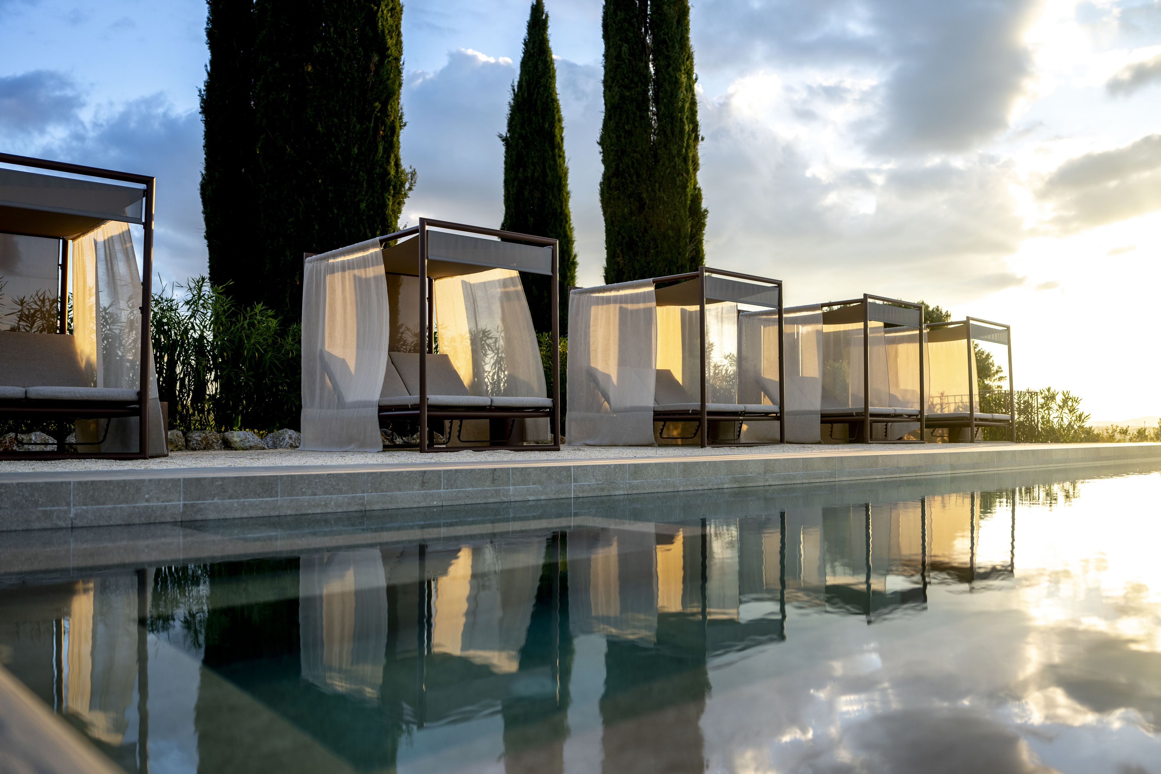 A poolside area with four covered seating areas, each with a cushioned bench and a transparent canopy.