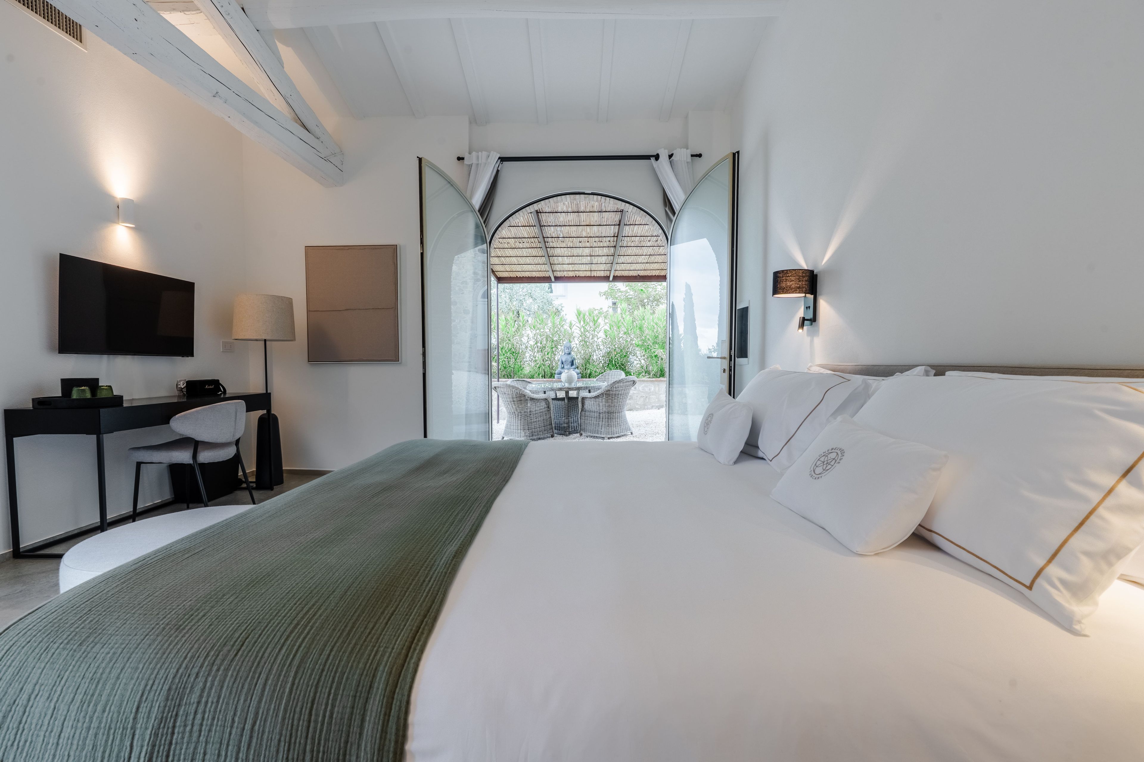 A modern bedroom with a large bed, a desk, a chair, and a television.