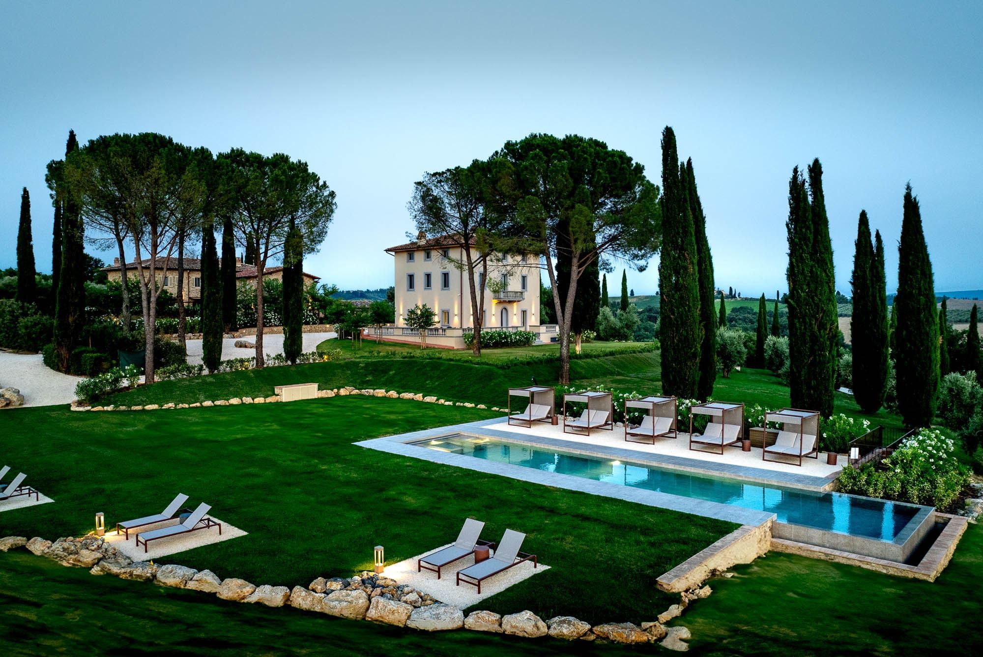 A pool area with lounge chairs, a well-manicured lawn, and a large building in the background.