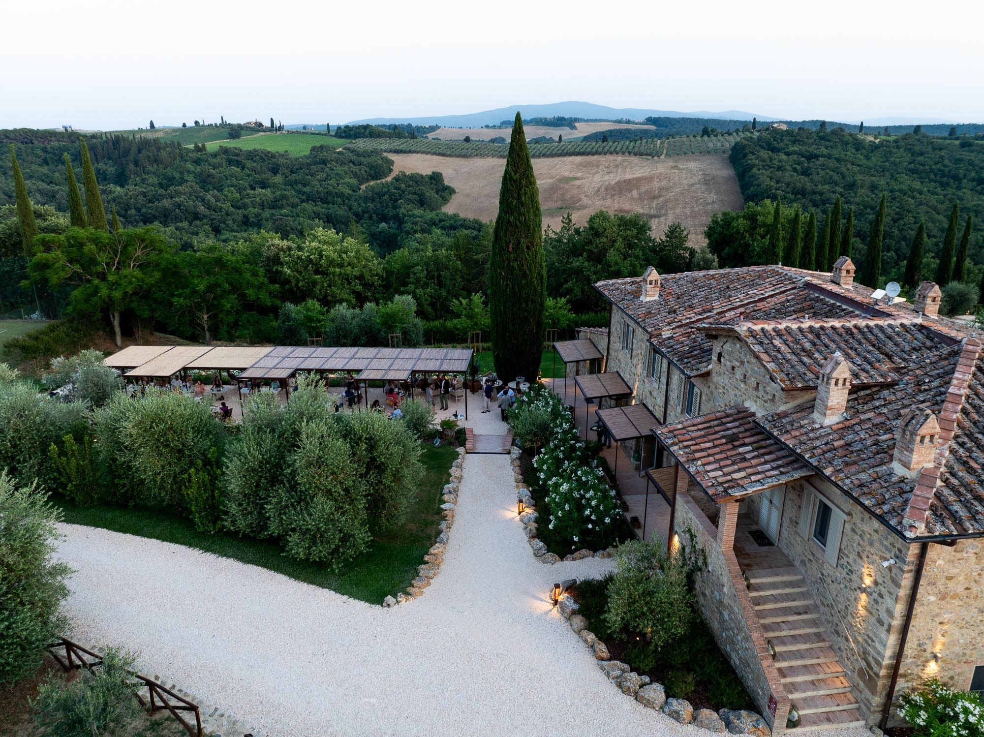 A stone building with a tiled roof, surrounded by greenery and a gravel path leading to a covered outdoor area.