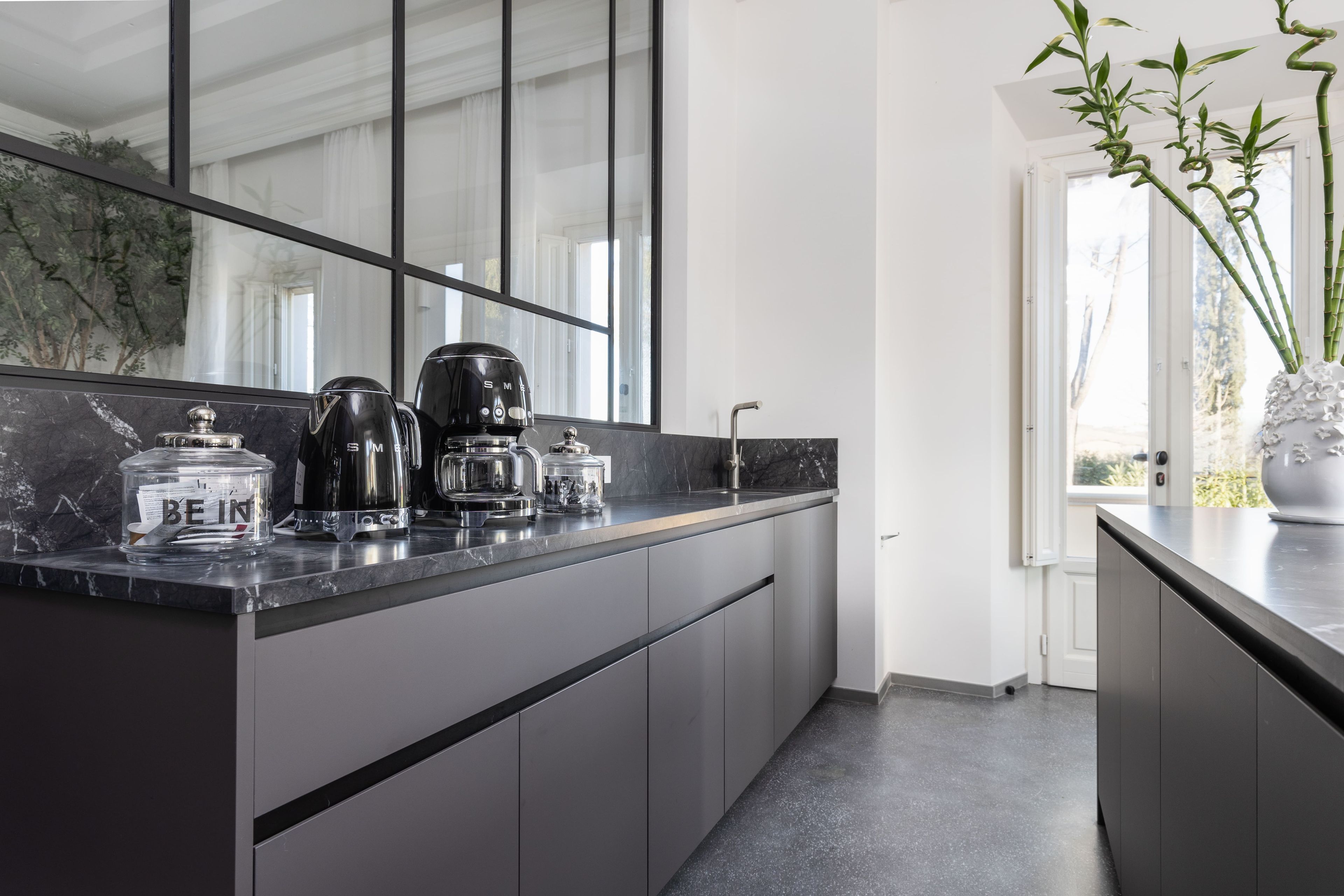 A modern kitchen with a dark countertop, stainless steel appliances, and a large window.