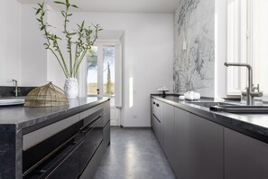 Ett modernt kök med en väggbeklädnad av marmor, rostfria köksmaskiner och ett stort fönster.