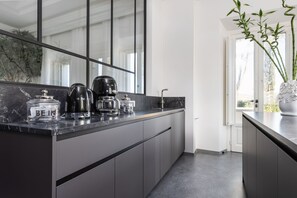 Ett modernt kök med en mörk bänkskiva, rostfria vitvaror och ett stort fönster.