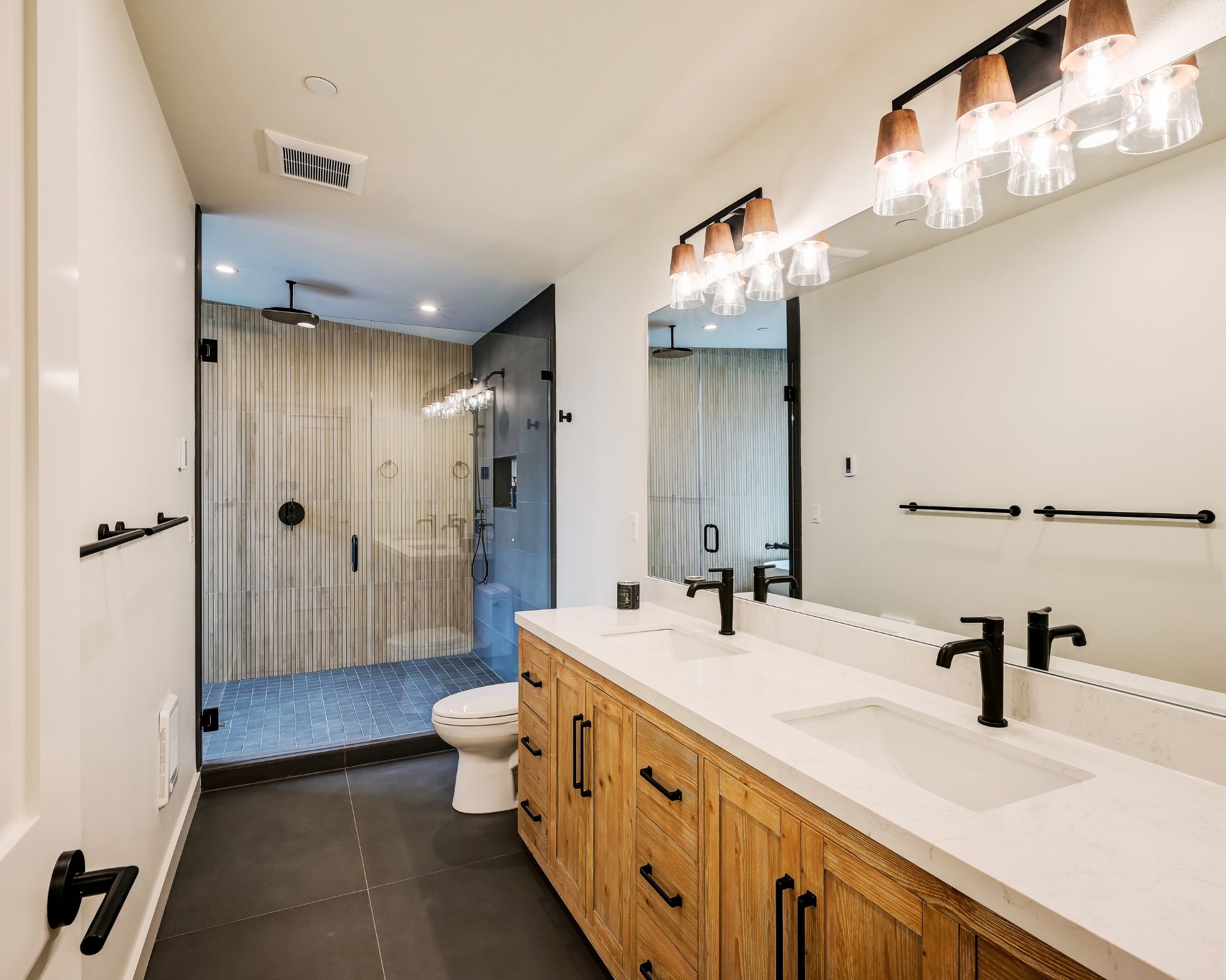 A modern bathroom with a large mirror, dual sinks, and a shower area.