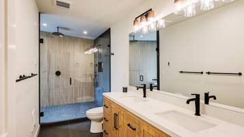 A modern bathroom with a large mirror, dual sinks, and a shower area.