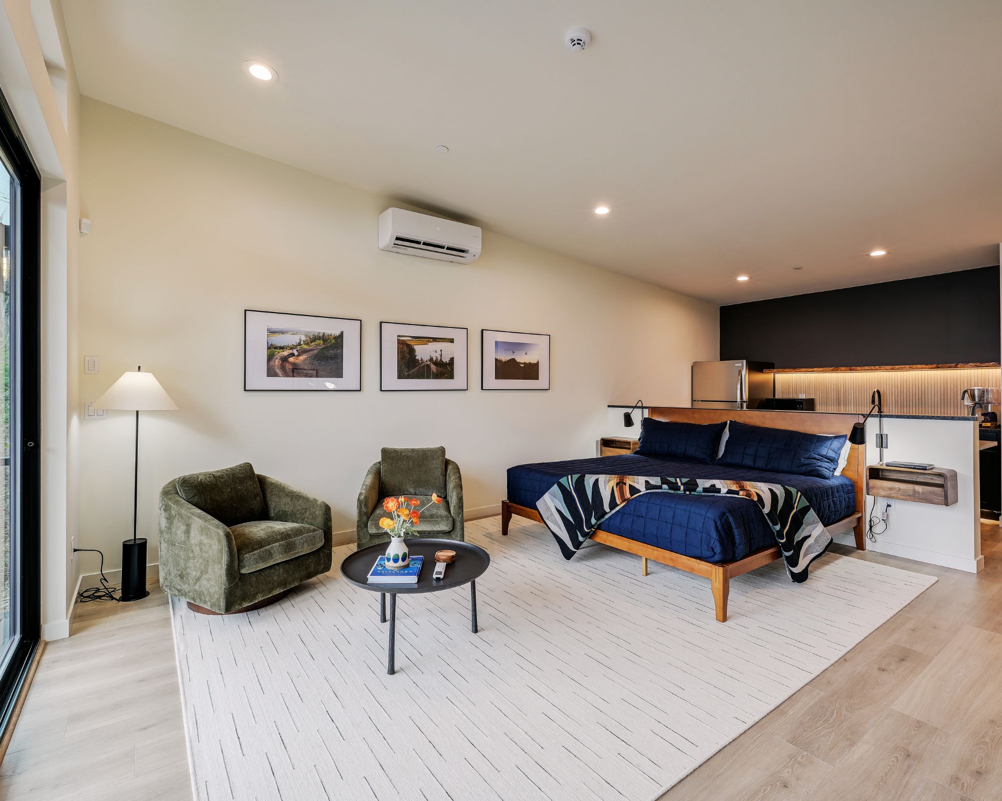 A modern bedroom with a bed, two chairs, a coffee table, and artwork on the wall.