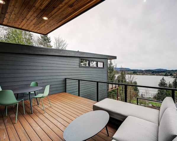 A modern outdoor deck with a wooden floor, a sofa, and two chairs.