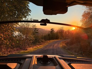 A vehicle's interior with a view of a rural road and sunset.