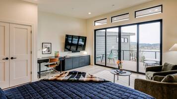 A modern bedroom with a large bed, a desk, a TV, and a balcony with a view.