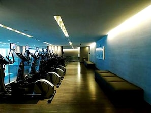 A gym with stationary bikes arranged in a row, a bench along the wall, and a corridor leading to an exit. - 50th Floor Penthouse. 2 Bedroom 2 Bath. Ocean/Beach. Now to 12/31/26 & 4/1/27 on (Hallandale Beach)