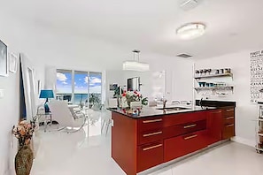 A modern kitchen with a central island, a dining area with a table and chairs, and a large window providing natural light. - 50th Floor Penthouse. 2 Bedroom 2 Bath. Ocean/Beach. Now to 12/31/26 & 4/1/27 on (Hallandale Beach)