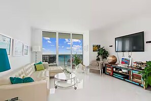 A modern living room with a sofa, coffee table, and a flat-screen TV mounted on the wall. - 50th Floor Penthouse. 2 Bedroom 2 Bath. Ocean/Beach. Now to 12/31/26 & 4/1/27 on (Hallandale Beach)