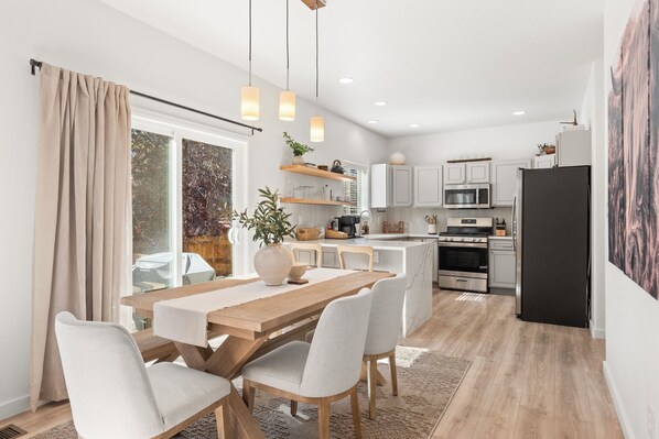 A modern kitchen with white cabinets, a black refrigerator, and a wooden dining table with chairs.