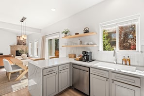 A modern kitchen with a dishwasher, a coffee maker, and a window with a view of trees.