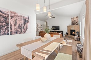 A modern living room with a fireplace, a dining area with a large table, and a television in the background. - Fairway & Fly at Sopris - Fishing, Golf, & Hot Tub (Carbondale)